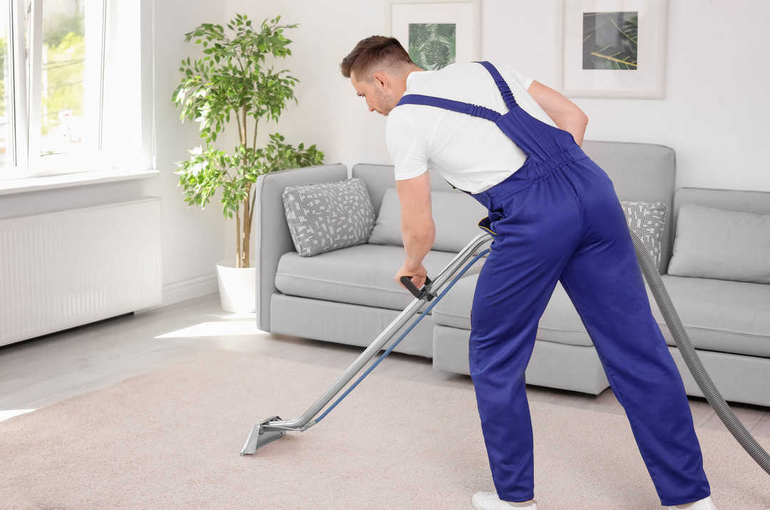 Male worker removing dirt from carpet with professional vacuum cleaner indoors