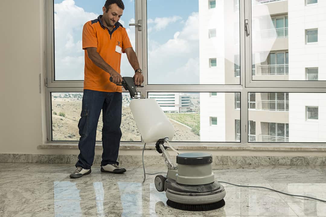 Worker wearing uniform cleaning marble floor with buffer