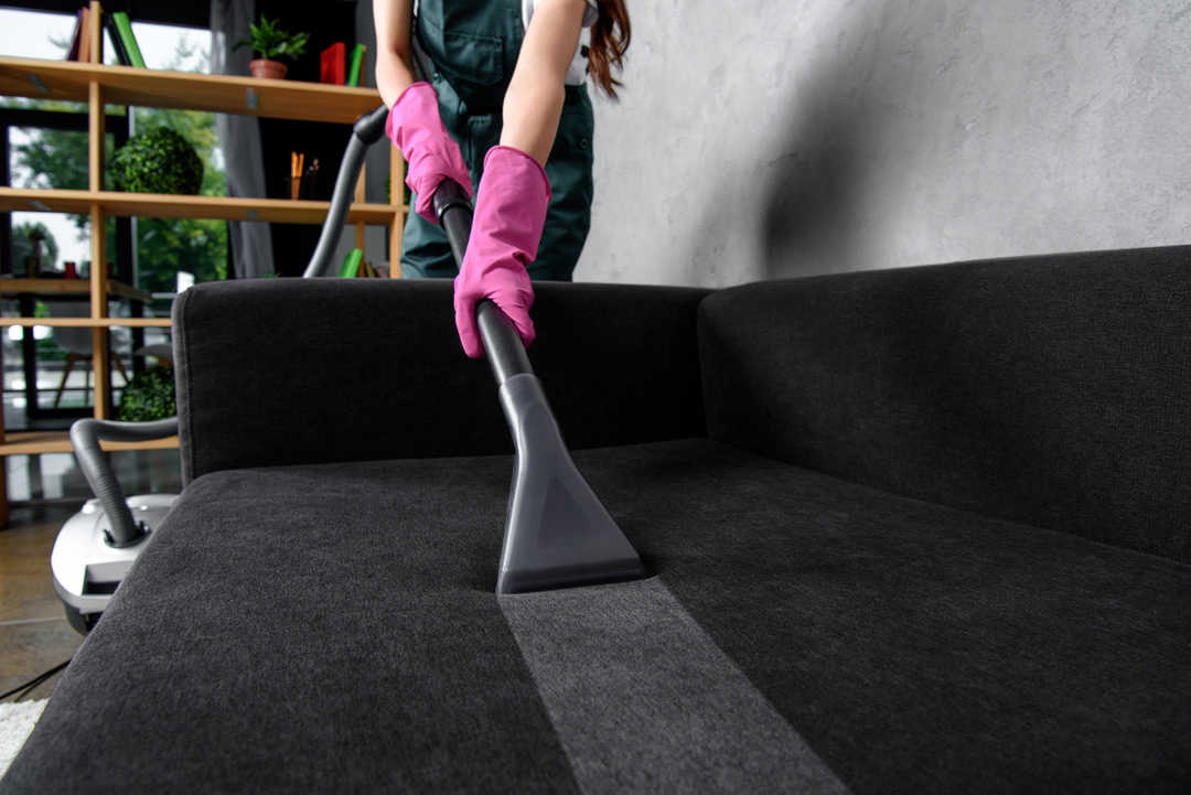 partial view of woman in rubber gloves cleaning furniture with vacuum cleaner
